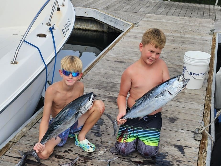 Two boys holding large tuna fish on a wooden dock near a boat