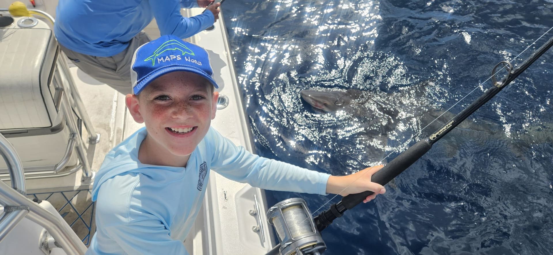 Young angler smiling while reeling in a fish on a kids' fishing charter off Lake Worth