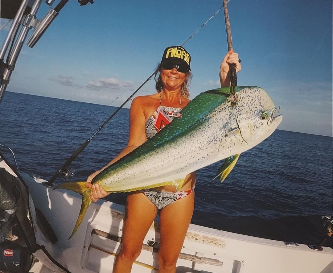 A woman on a fishing boat holds a large mahi-mahi at sea