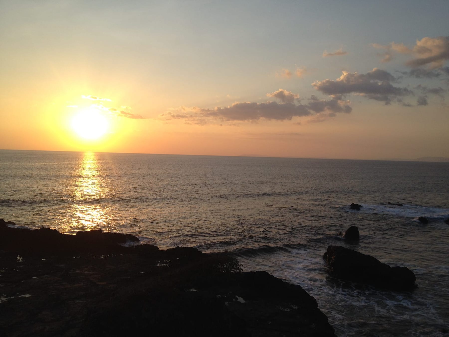 The sun low over the Pacific beside dark rocks