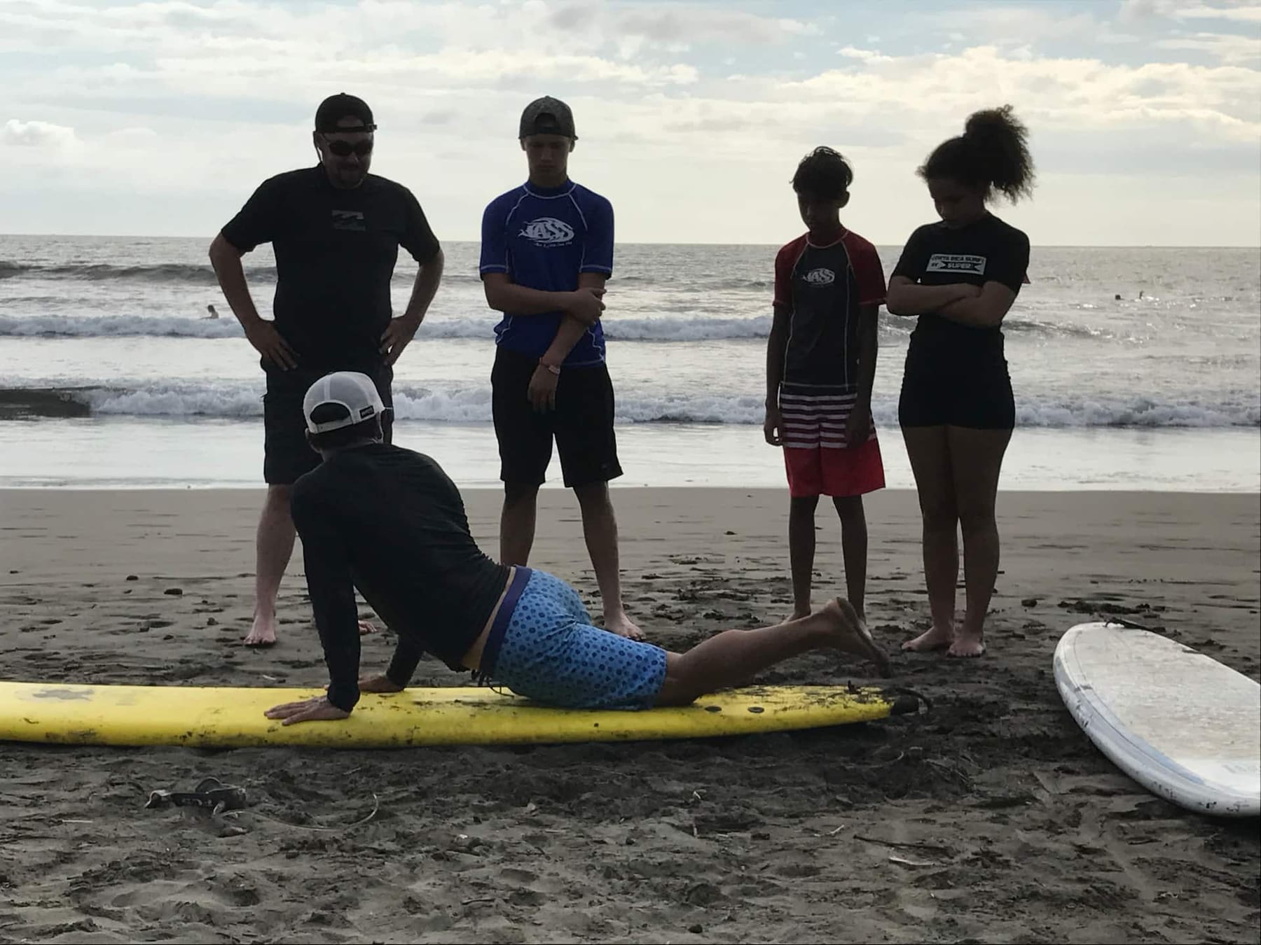A surf lesson on the beach, a student practicing a pop-up on a board