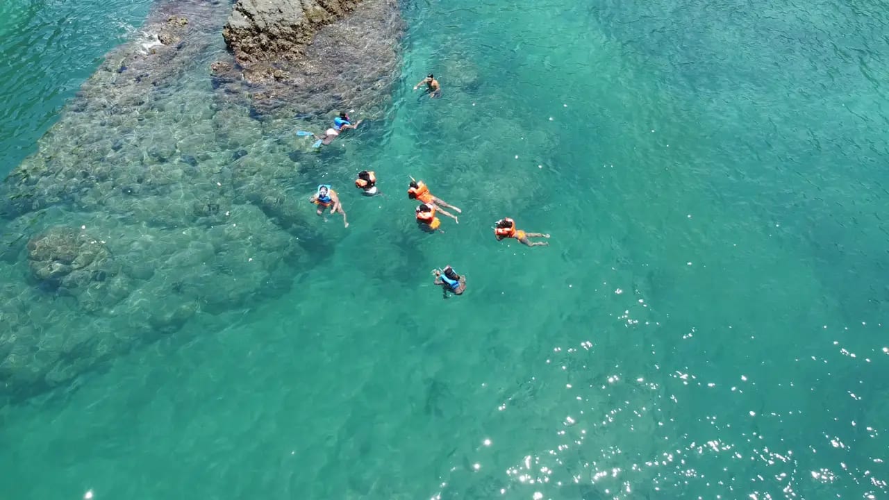 Snorkelers in clear turquoise water beside the rocks