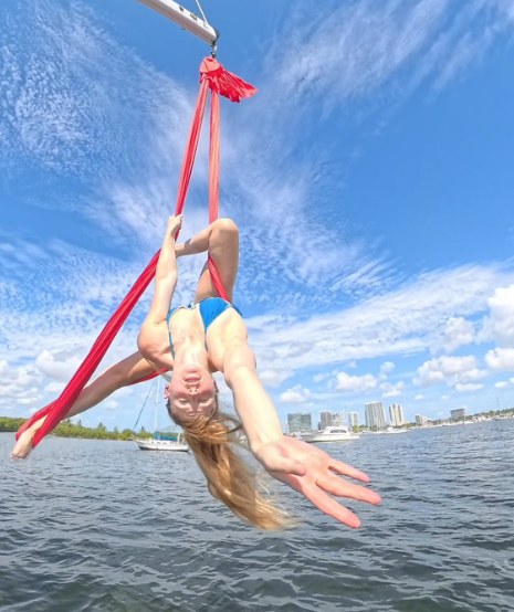 An aerialist on red silks hung from the mast over the bay