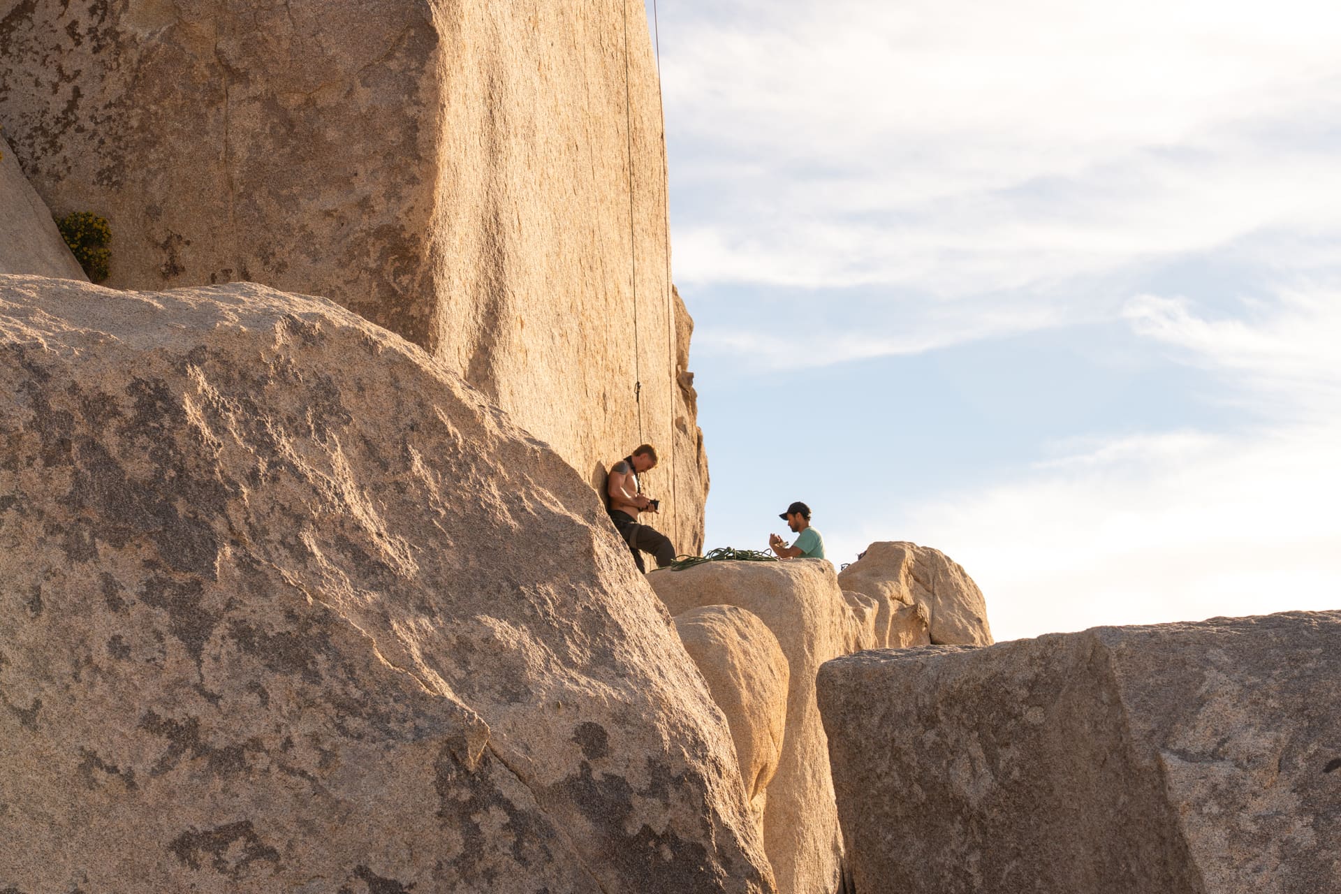 Two rock climbers resting with gear on a sunny granite rock formation