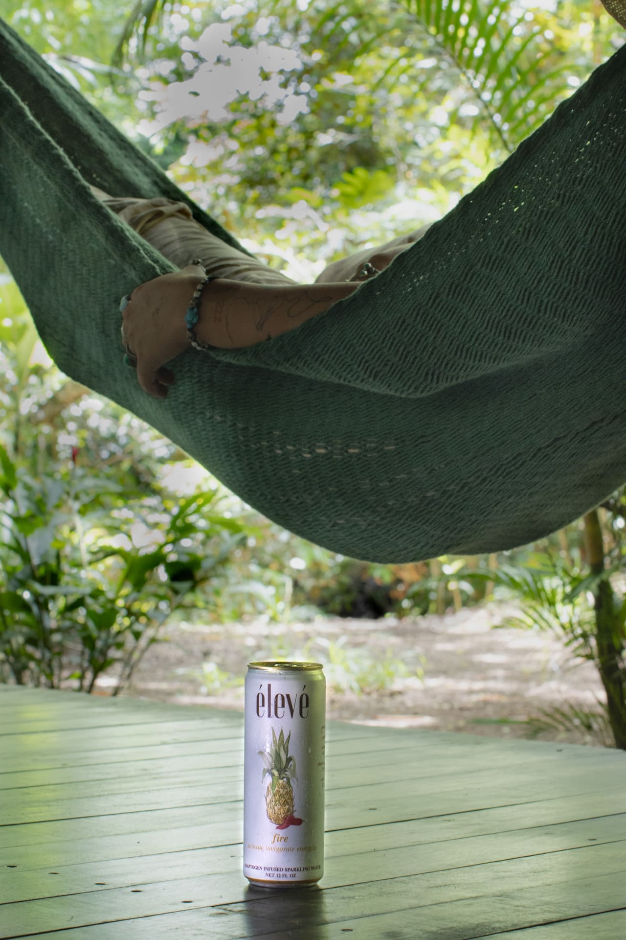 A can of élevé sparkling water sits on a wooden deck below a green hammock