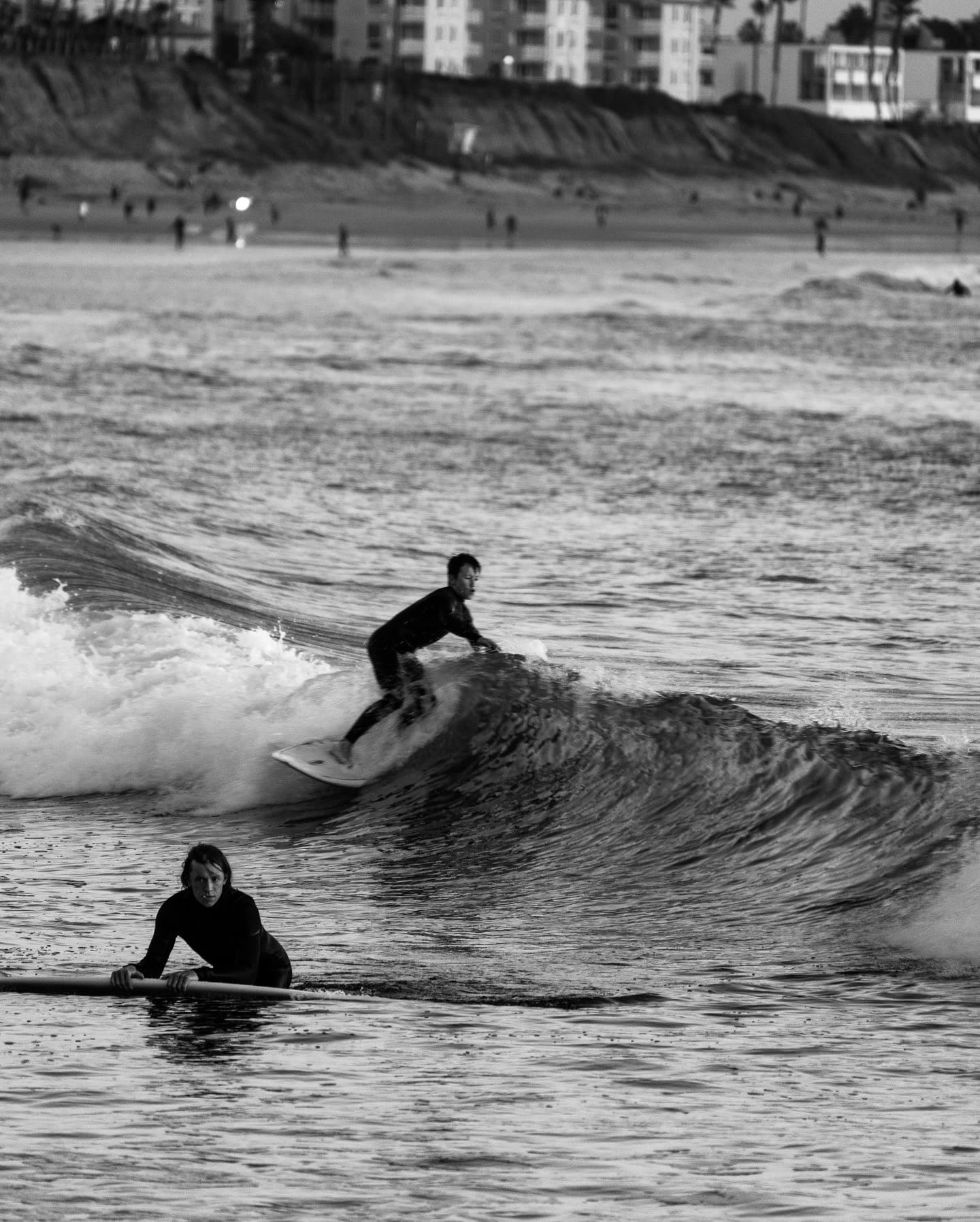 A surfer riding a wave while another surfer rests on a surfboard in the ocean