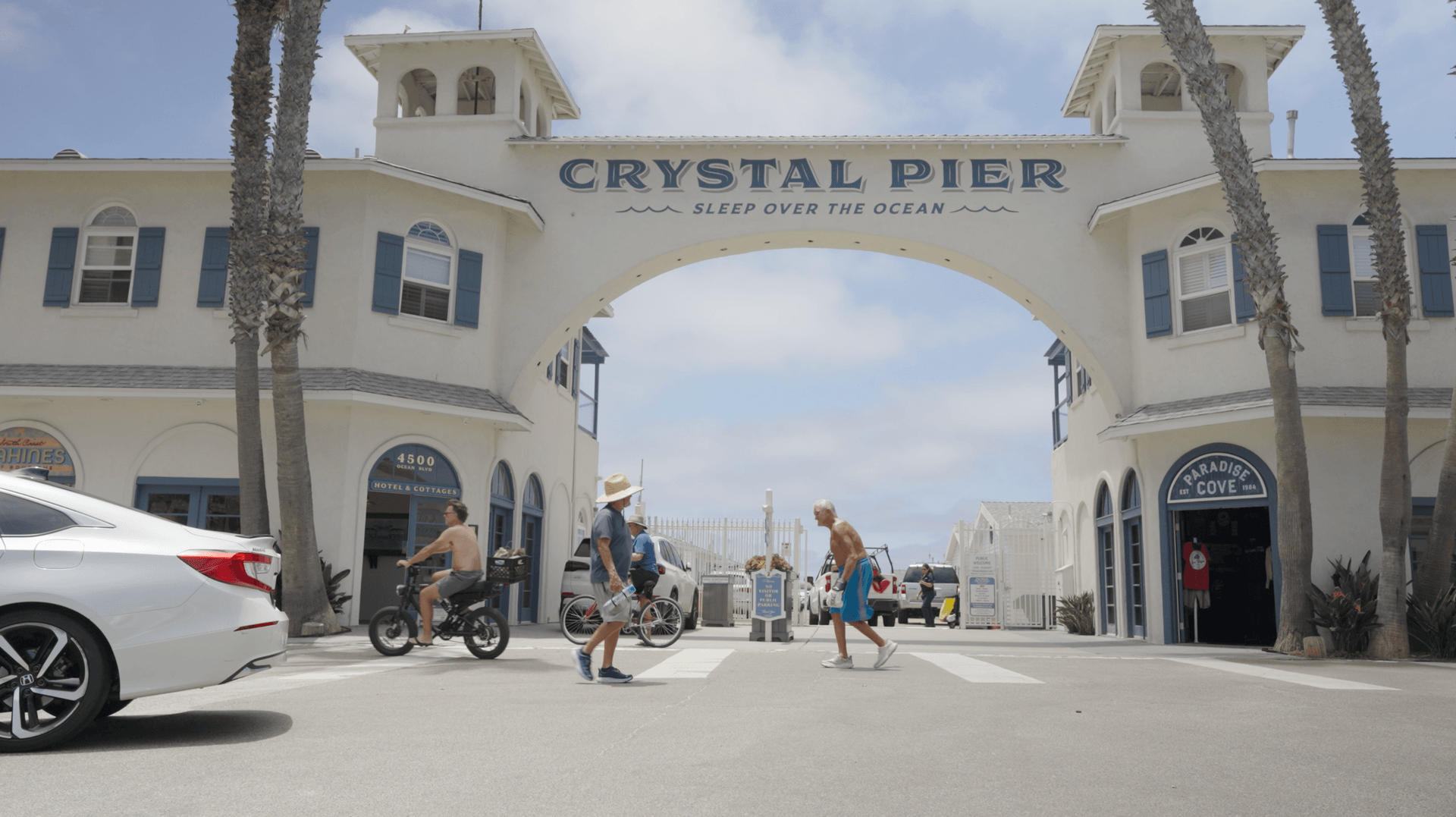 Pedestrians and cyclists pass beneath the Crystal Pier entrance arch in Pacific Beach