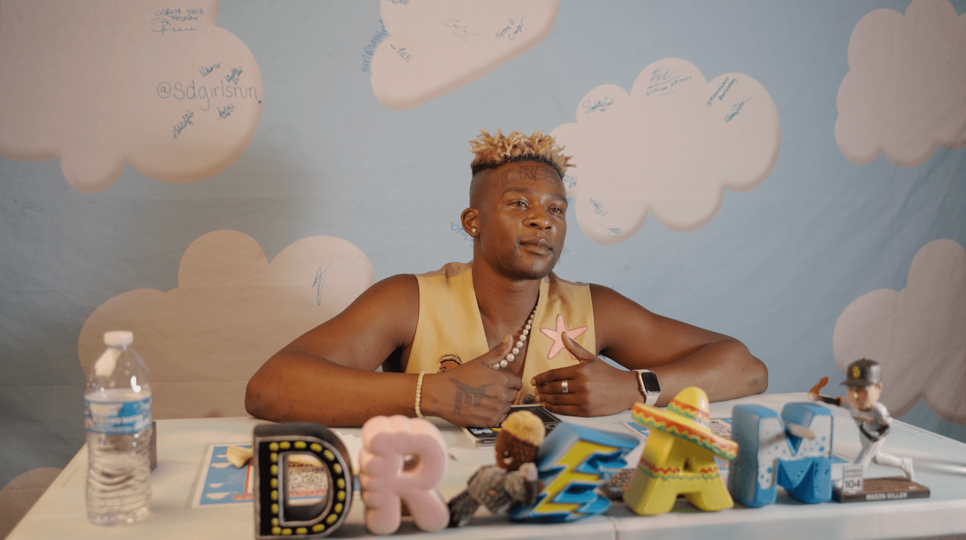 Man in yellow tank top sits at decorated table with colorful letter displays