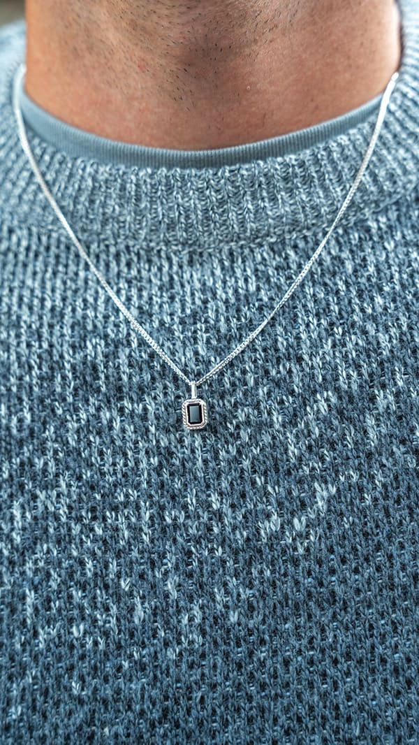 A man wearing a silver chain necklace with a small rectangular black stone pendant
