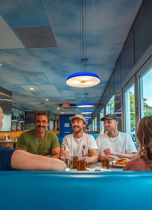 Friends sitting at a blue diner booth smiling and talking over coffee