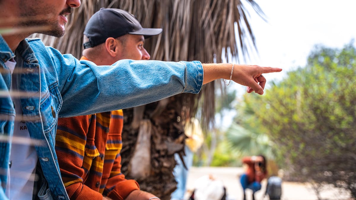 A man in a denim jacket points his finger outdoors beside another man