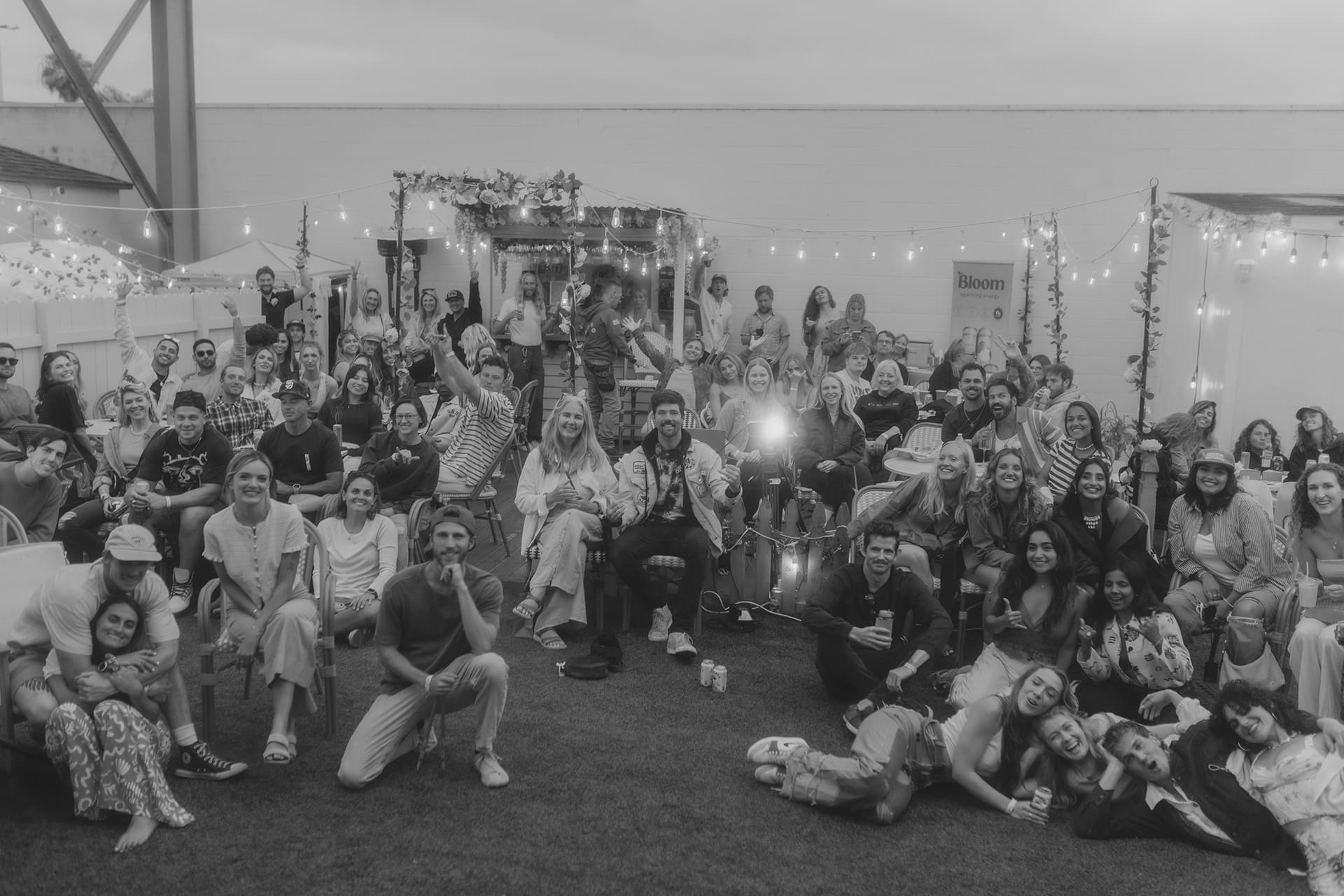 A large group of people posing together at an outdoor event under string lights