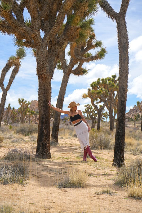 A woman in pink cowboy boots leans against a Joshua tree in the desert