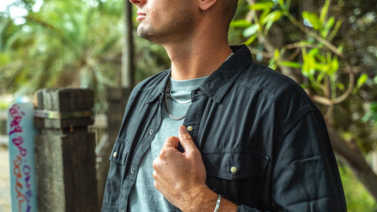 Man wearing an open black shirt over a grey t-shirt with silver chain necklaces