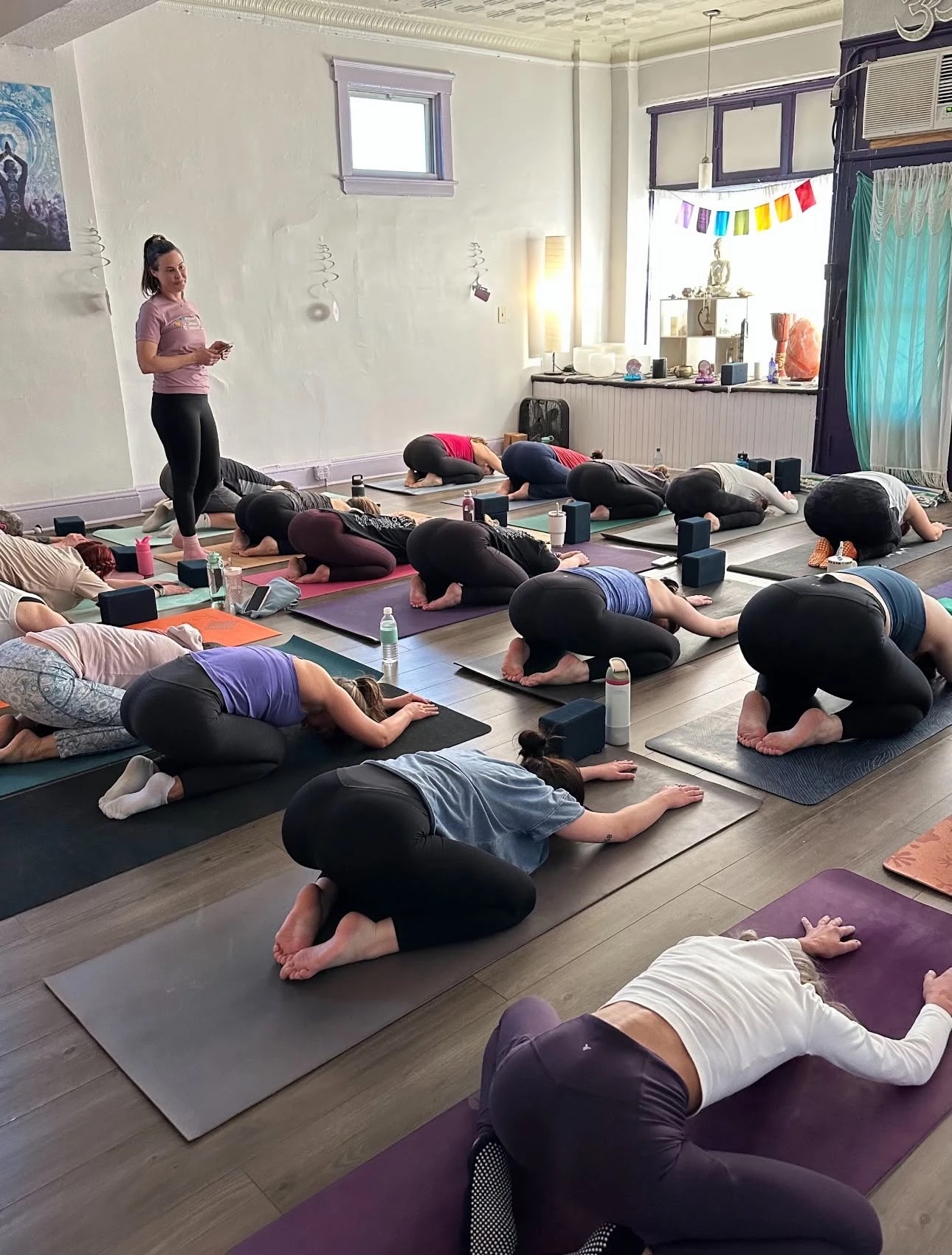 A full class resting in child's pose at Lakewood Yoga, the teacher standing among the mats
