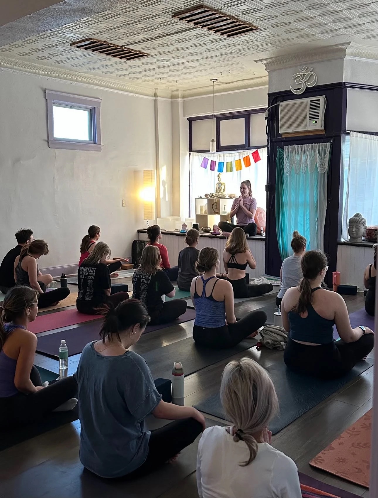 A seated class facing the teacher at the altar in the bay window at Lakewood Yoga