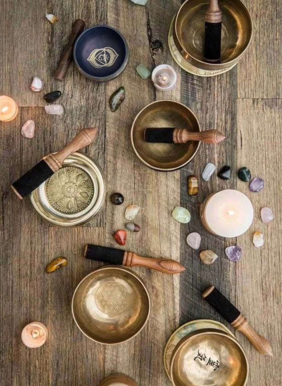 Singing bowls, candles and crystals laid out on a wood floor before sound healing