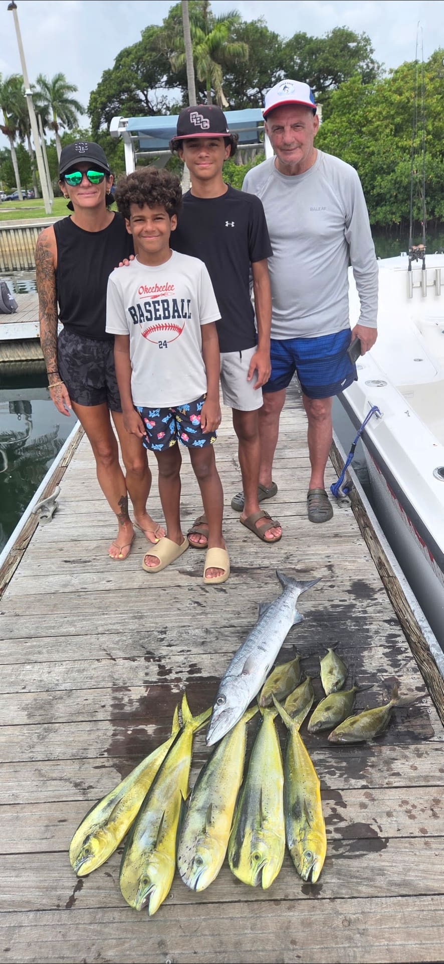 Four people pose on a wooden dock above a catch of mahi-mahi and barracuda