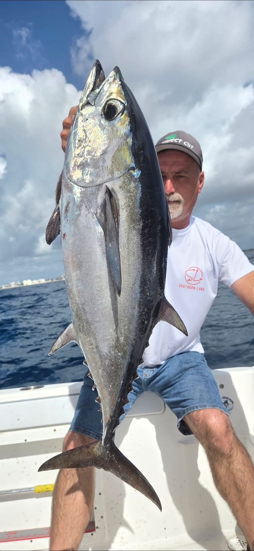 A man sitting on a boat holding up a large freshly caught tuna