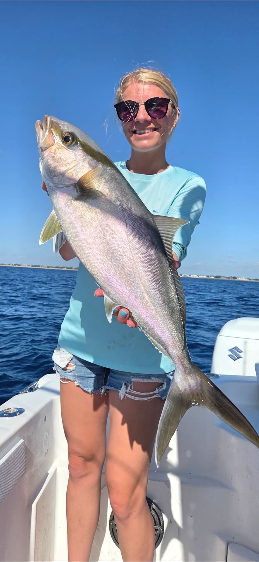 A smiling woman holding a large amberjack fish while on a boat at sea