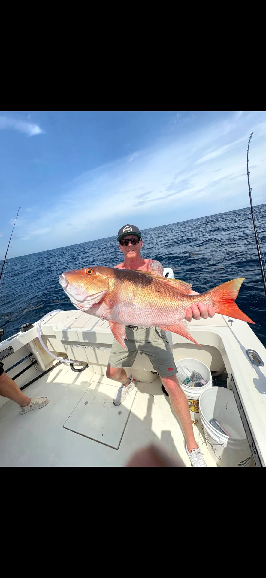 A man holds a large snapper fish while standing on a boat at sea