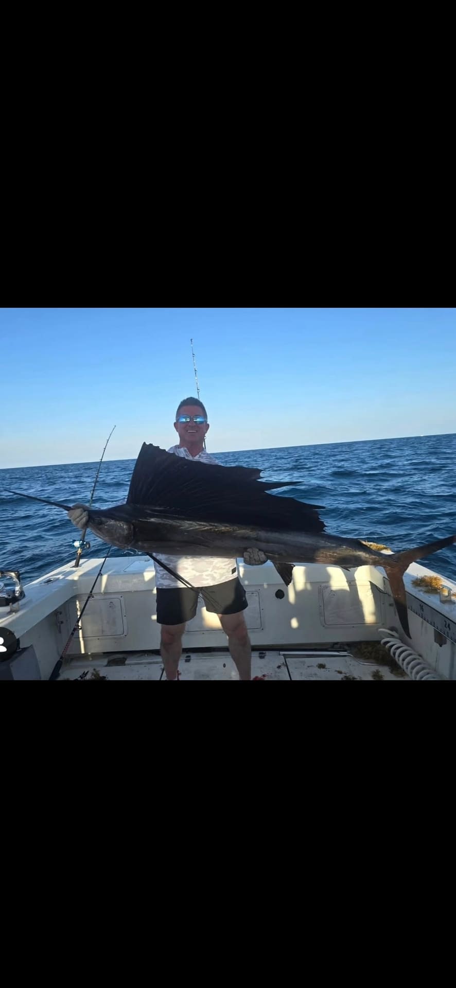 A smiling man on a boat holding a large sailfish with the ocean behind him