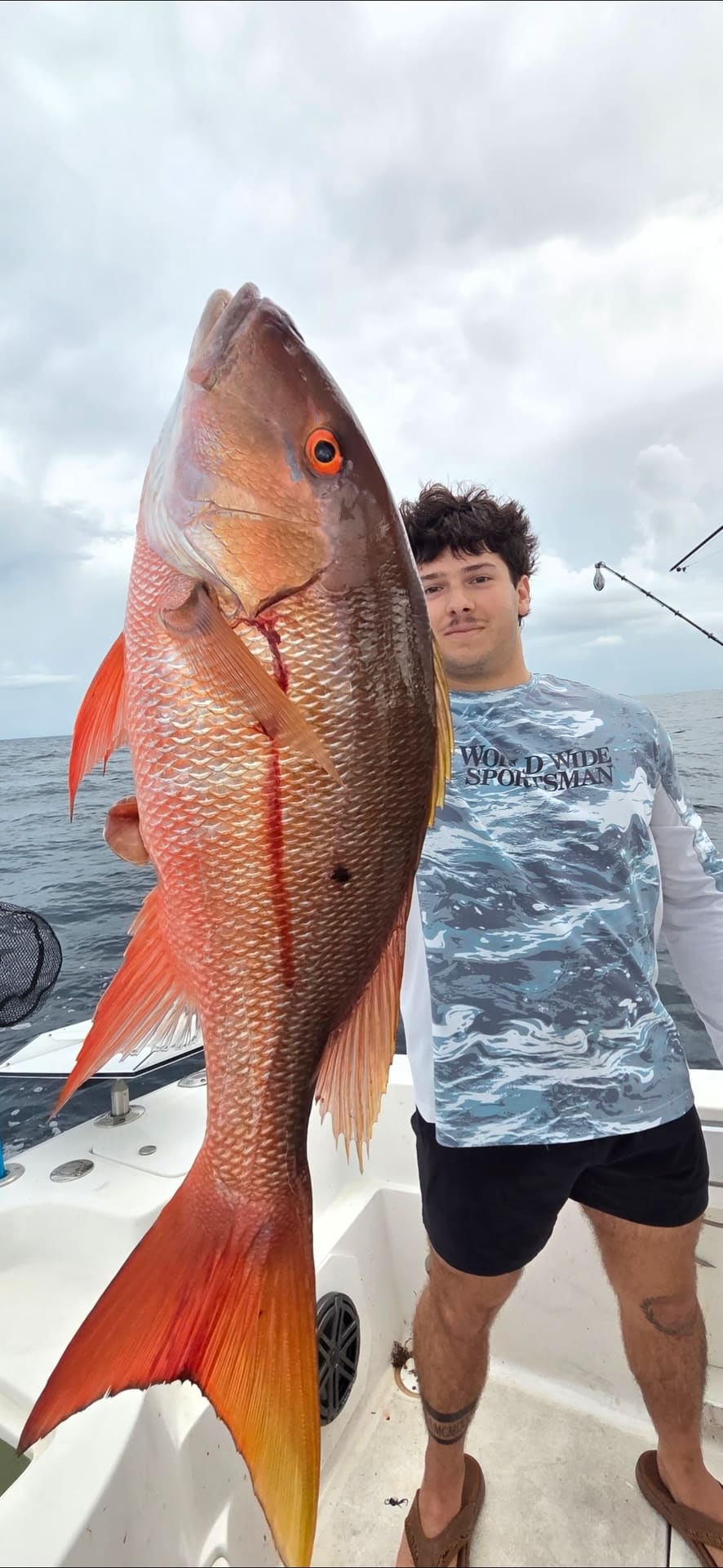 A man holding a huge red snapper on a fishing boat in the ocean