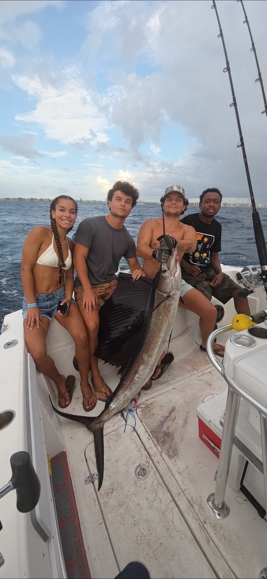 Four people on a fishing boat deck posing with a large sailfish