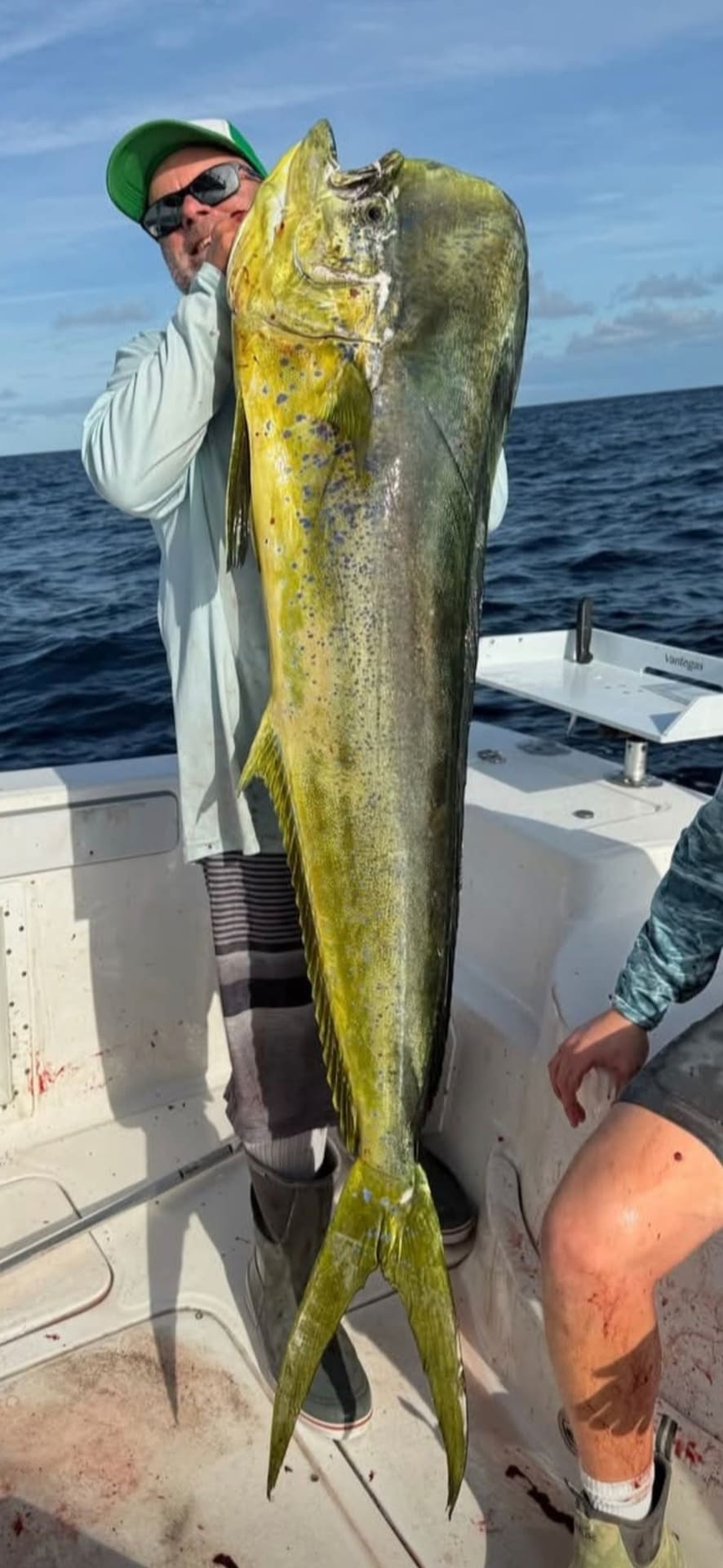 A fisherman on a boat holding up a large yellow and green mahi-mahi