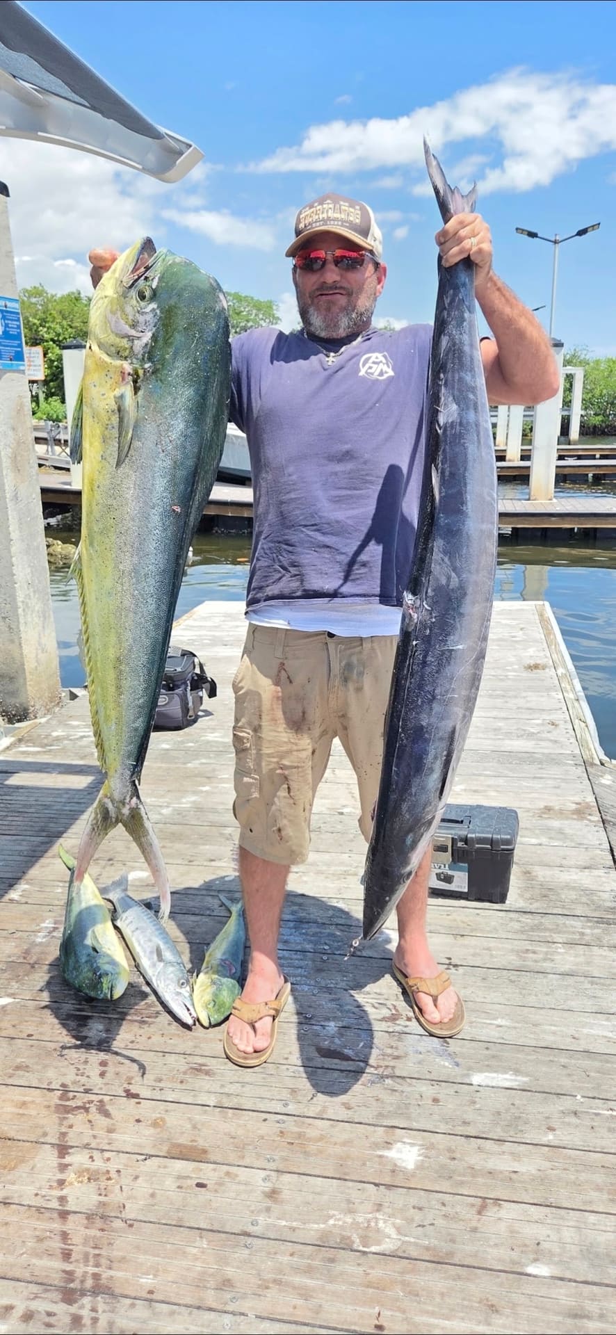 A man stands on a wooden dock holding up two large caught fish