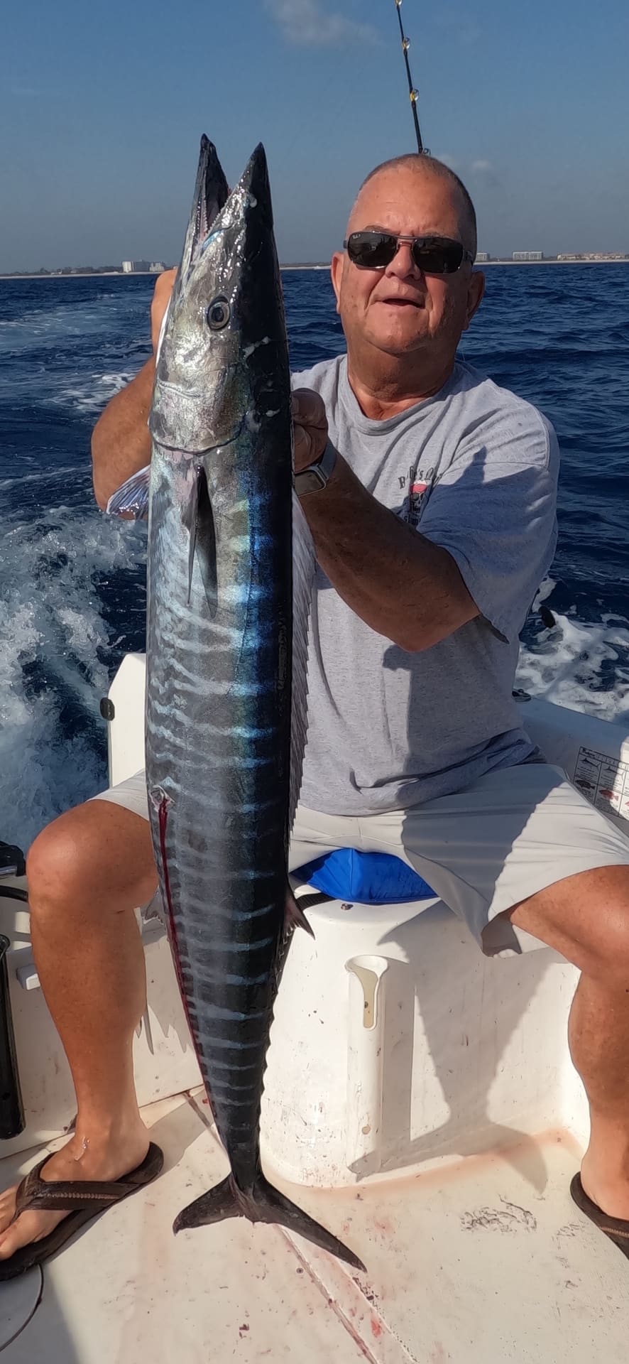 Man sitting on a boat holding up a large wahoo fish in the ocean