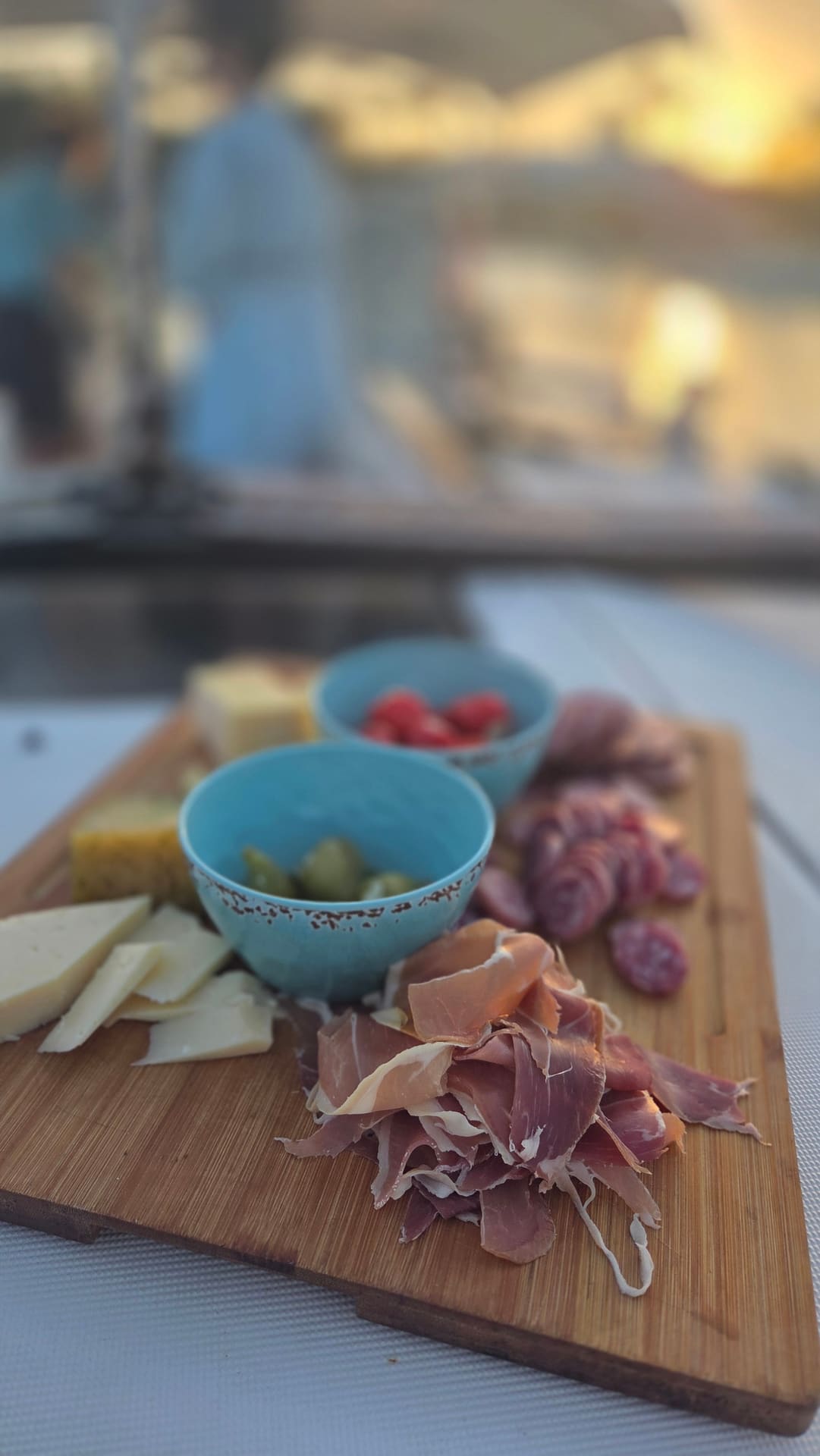 Charcuterie board with prosciutto, cheese, olives, and cherry tomatoes at sunset