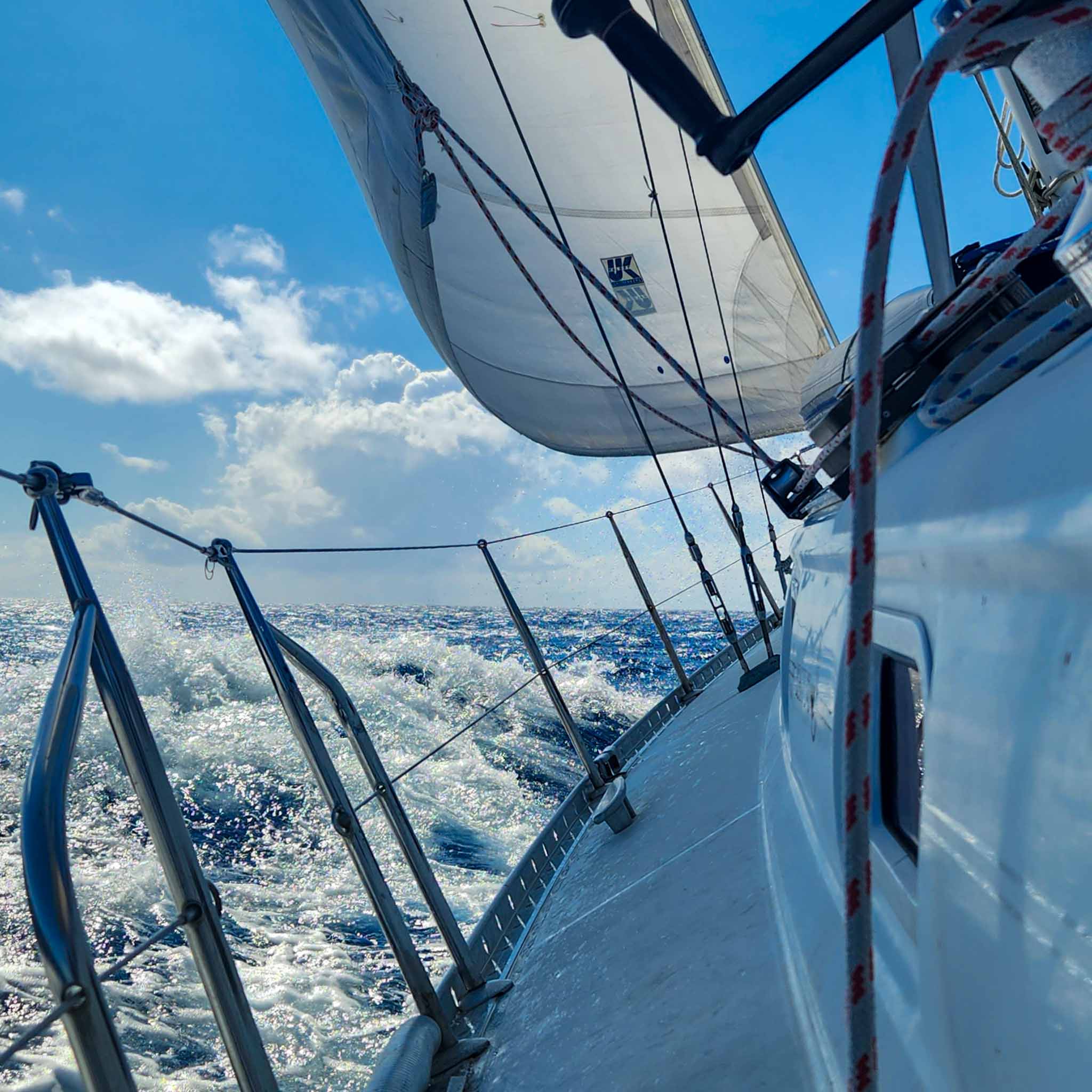 Sailboat heeling sharply through choppy blue ocean waves under a sunny sky