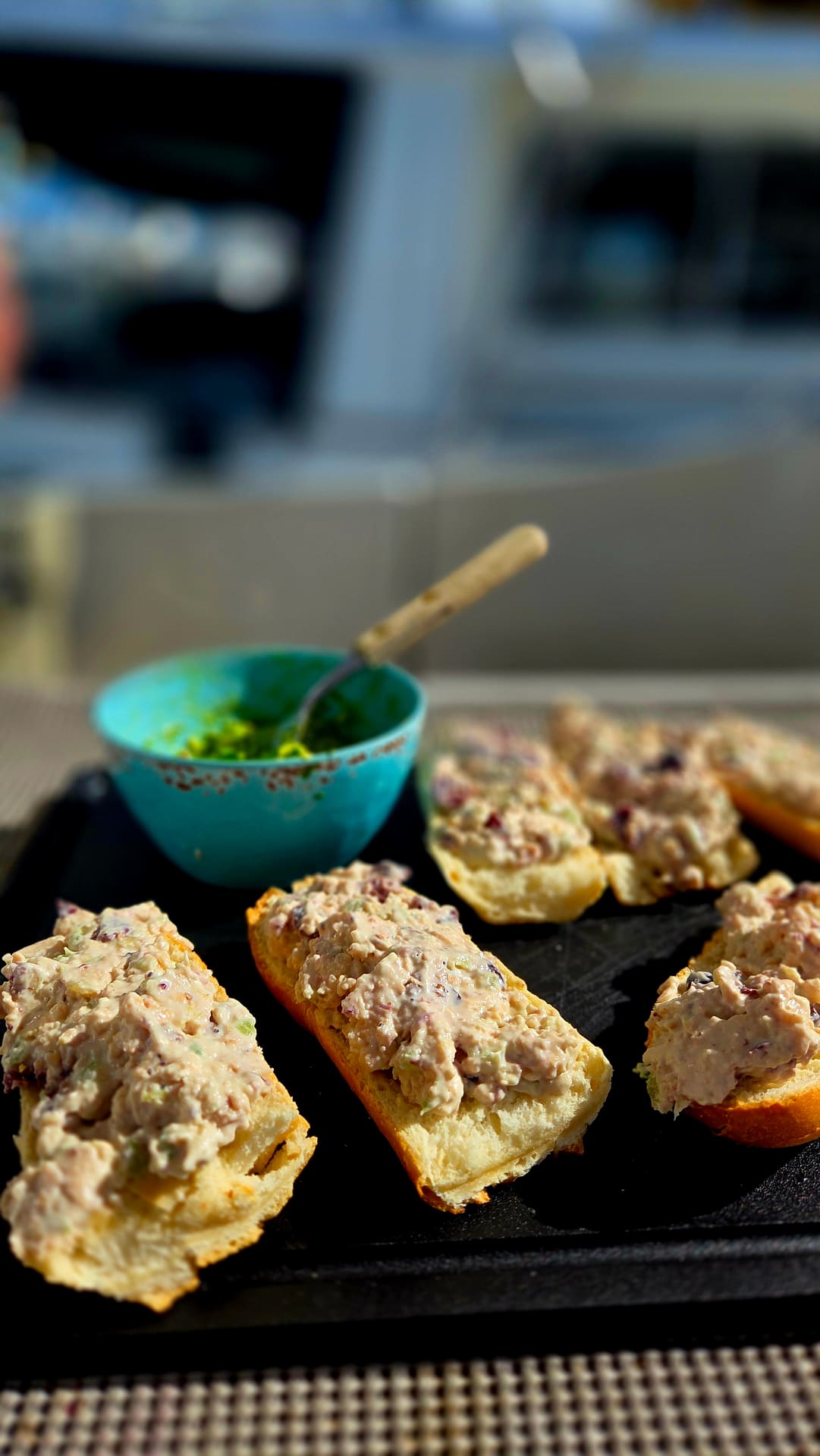 Crusty bread topped with creamy chicken salad alongside a blue bowl of green sauce