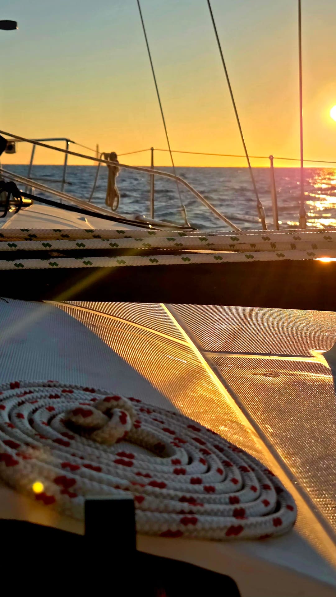 Coiled rope on sailboat deck glowing at golden sunset over calm sea