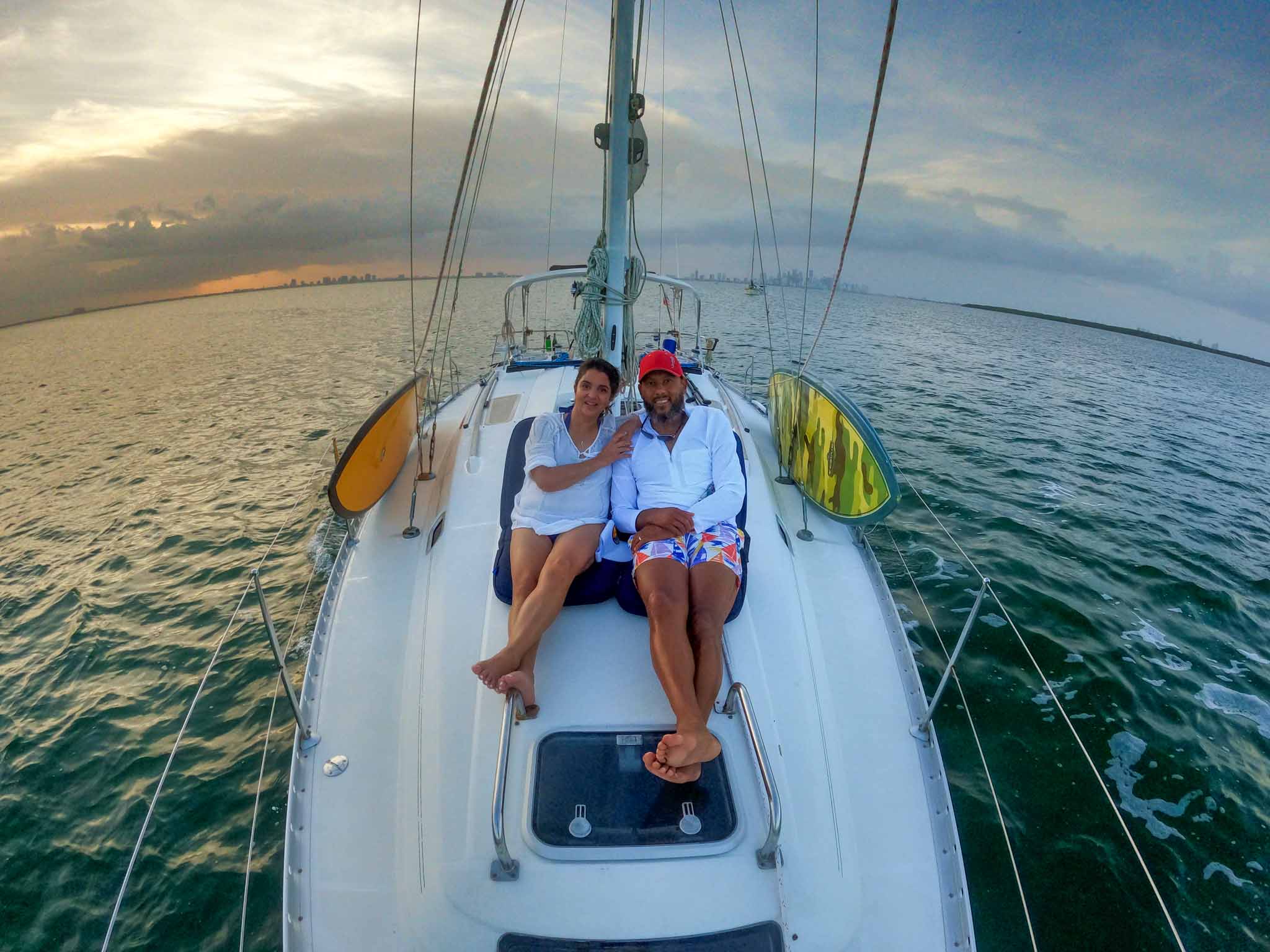 Couple relaxing on sailboat bow at sunset over calm ocean waters