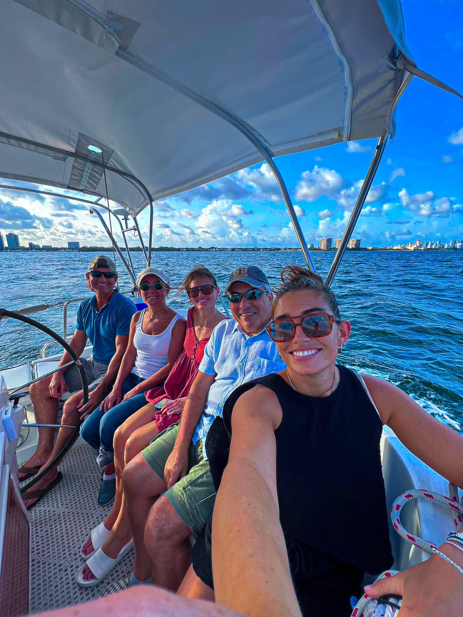 Five people smiling on a boat selfie with blue ocean skyline behind them