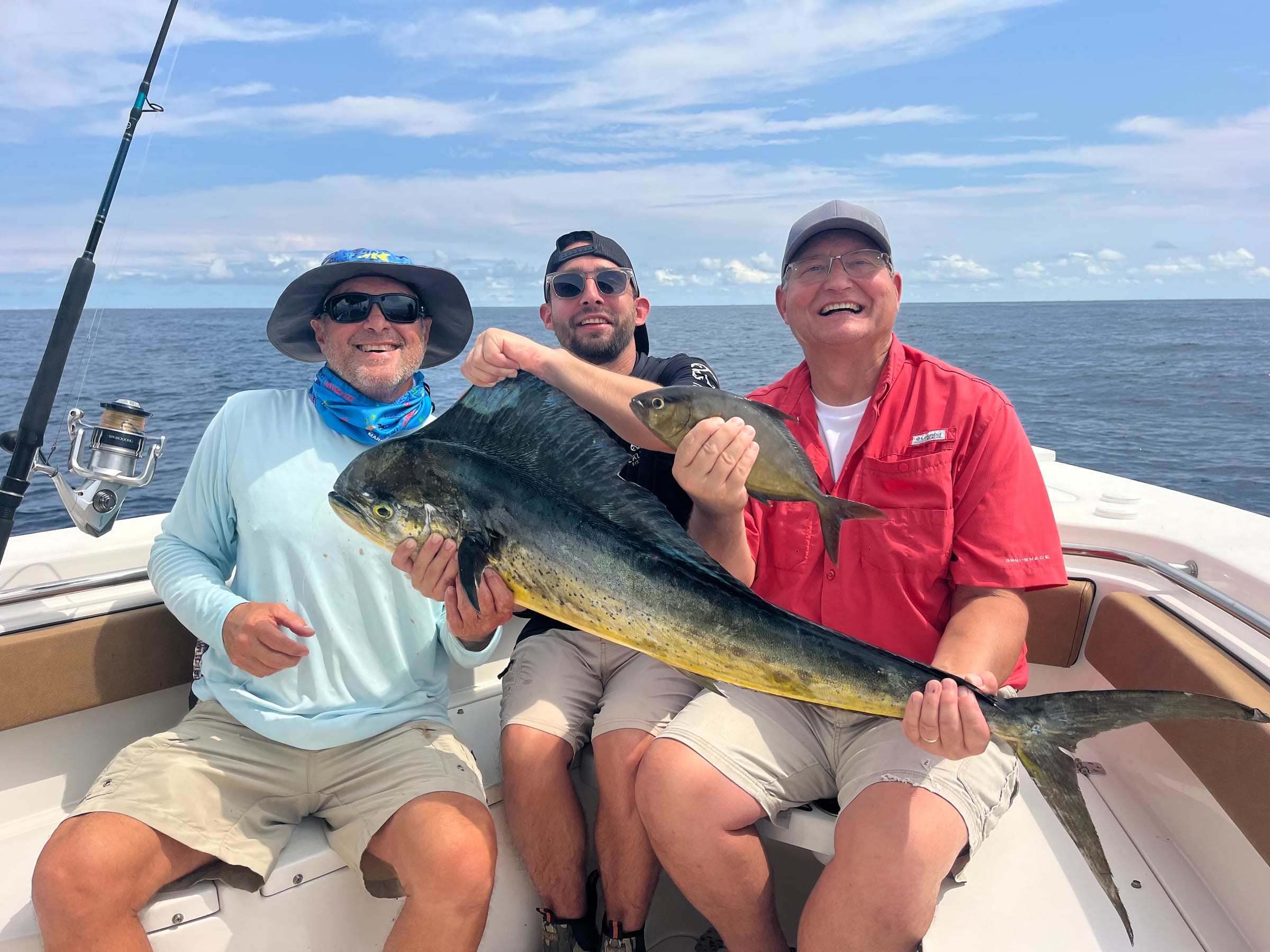 Three smiling men holding a large mahi-mahi on a fishing charter boat