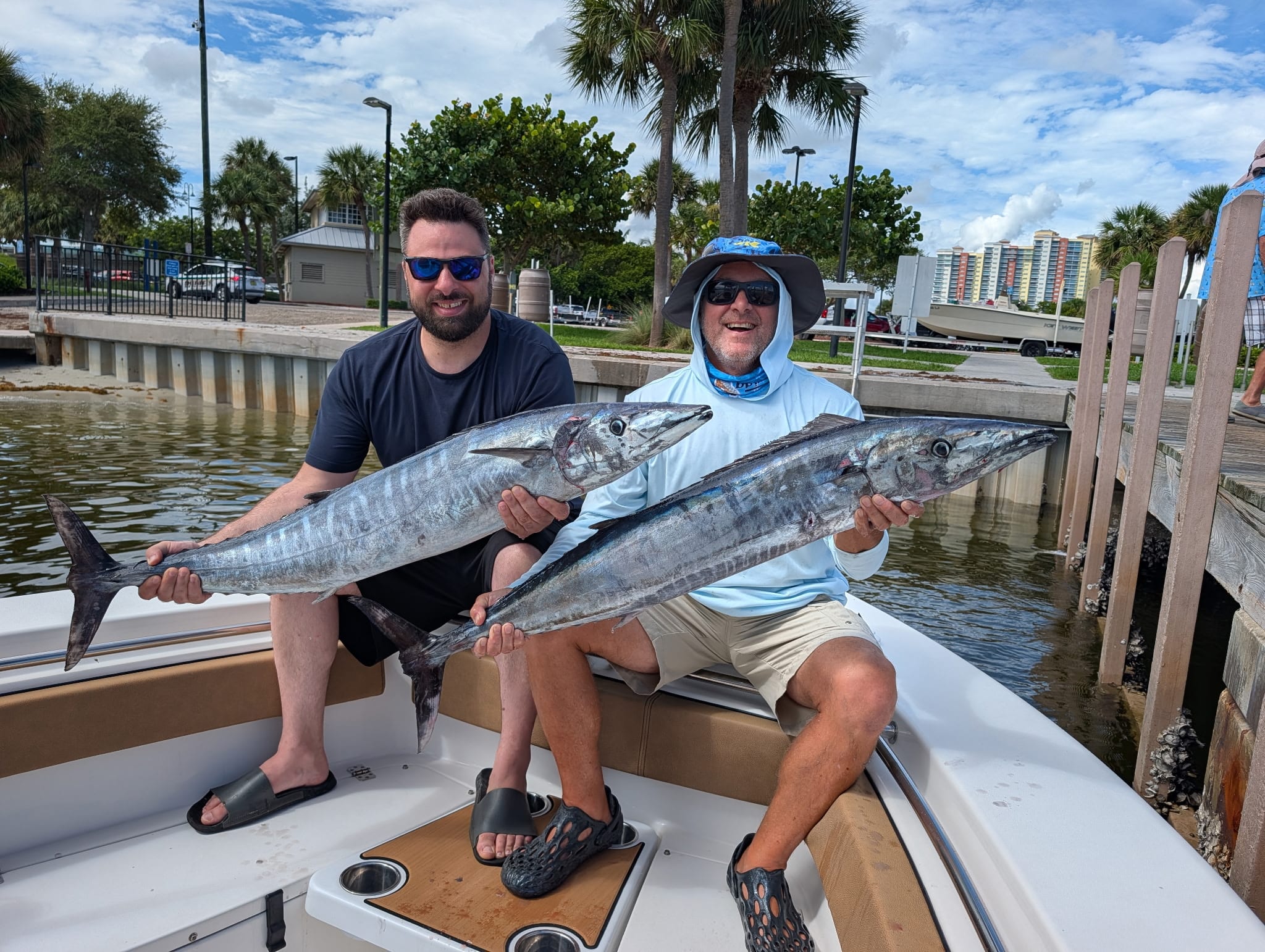 Two men on a boat holding large wahoo fish near a Florida dock