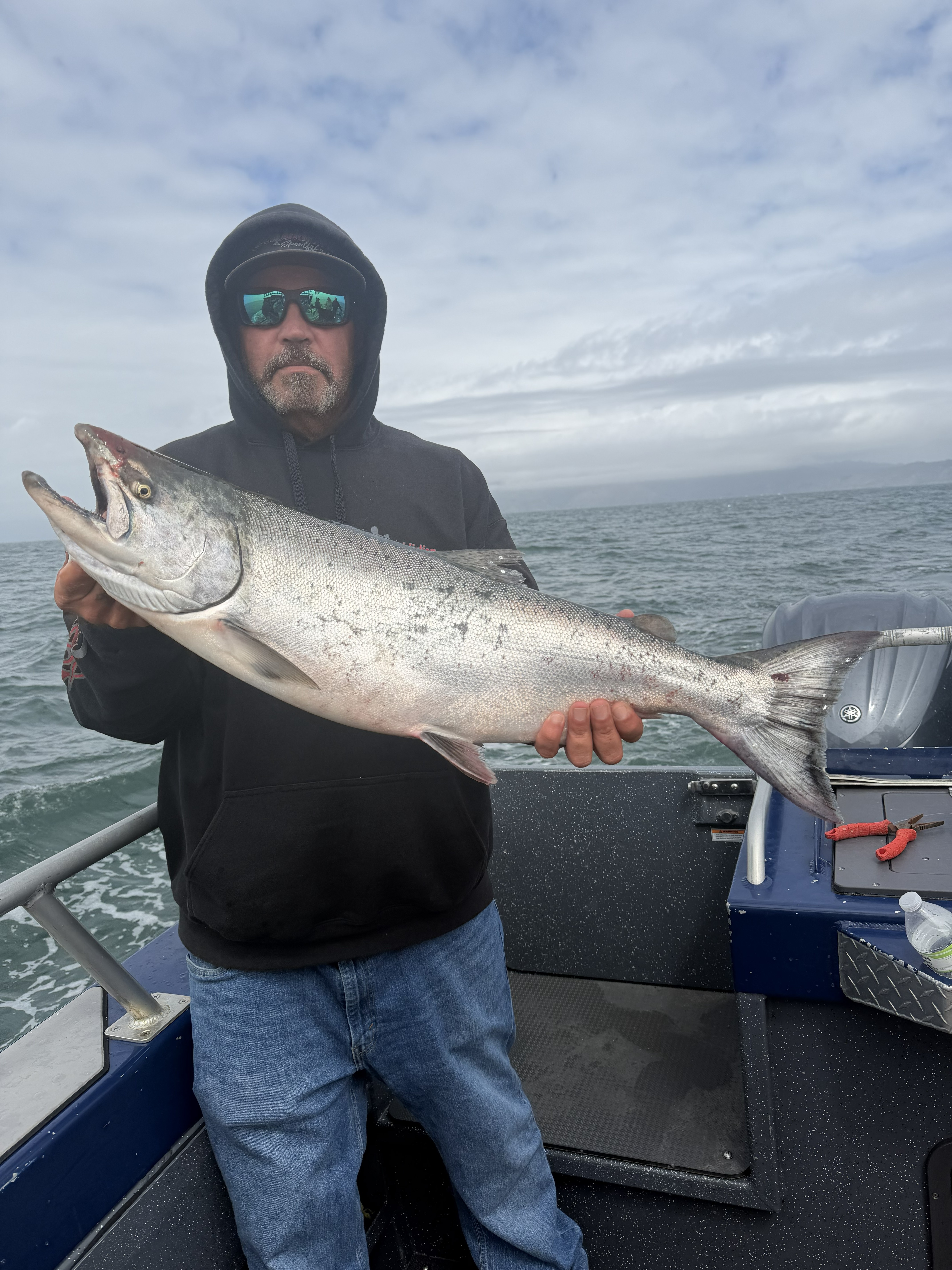 An angler in a hoodie holding a king salmon on deck
