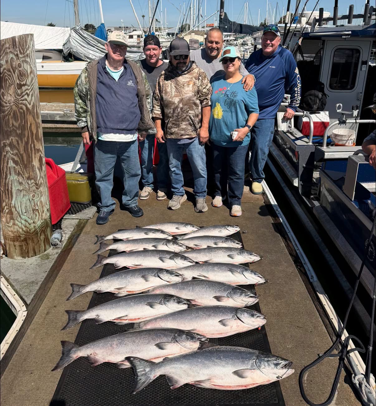 Six anglers on the dock behind two rows of king salmon
