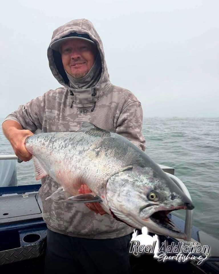 An angler in a hood holding a king salmon on a foggy day