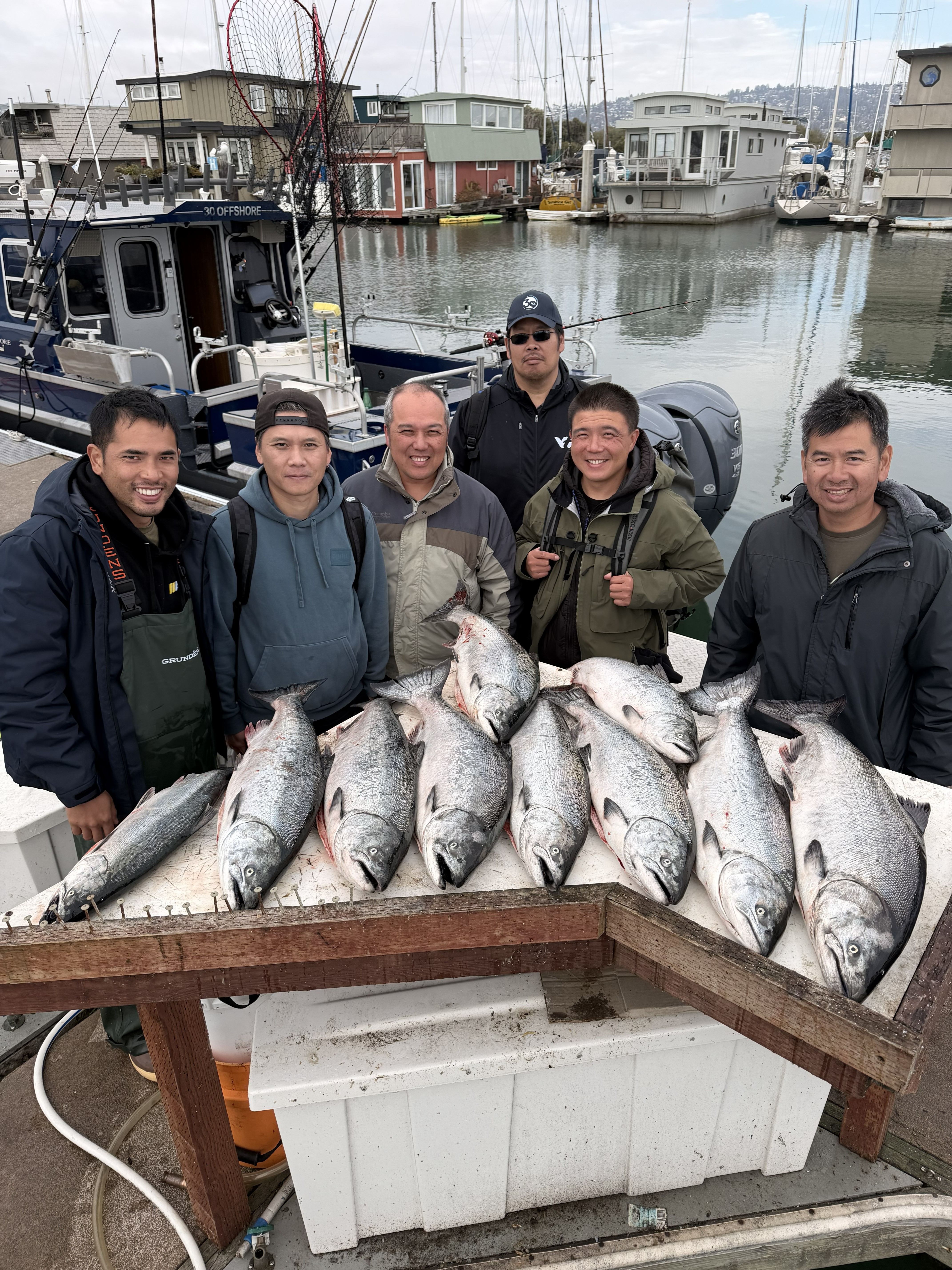 Six anglers on the dock behind a table of king salmon