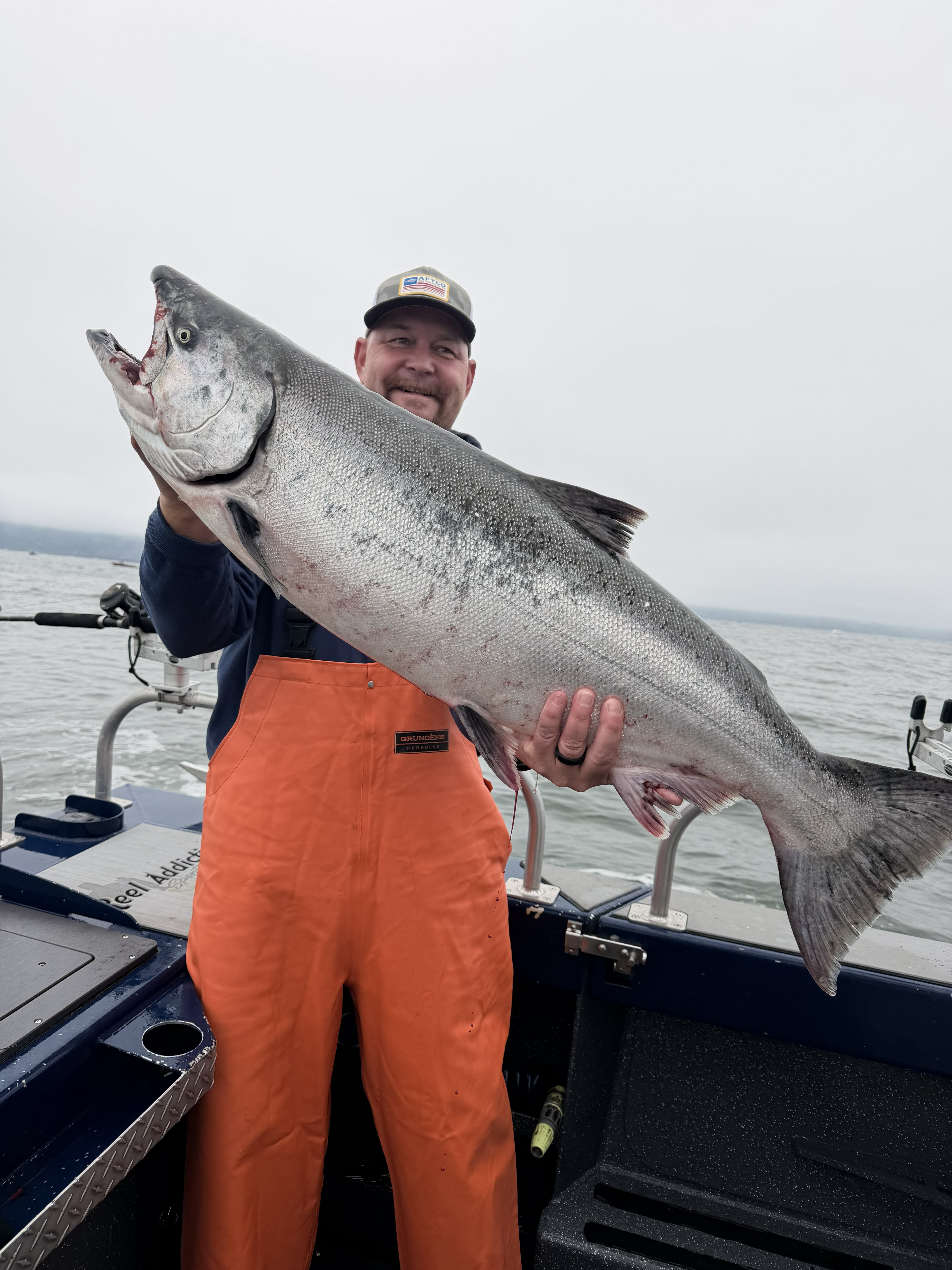 An angler in orange bibs holding a king salmon