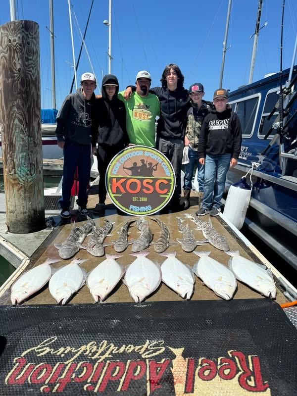 A kids' outdoor sportsman club group on the dock at Berkeley Marina behind a catch of halibut and leopard sharks laid out on the Reel Addiction mat