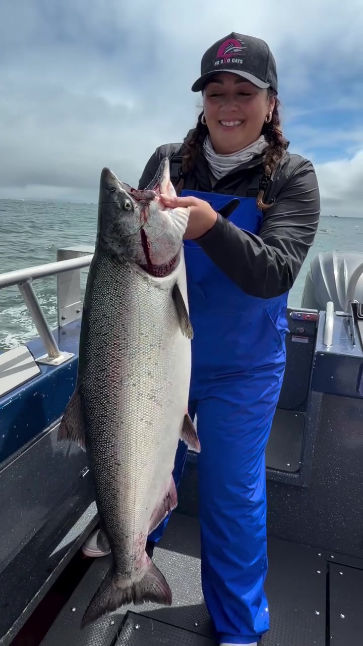A woman in bib overalls holding a king salmon