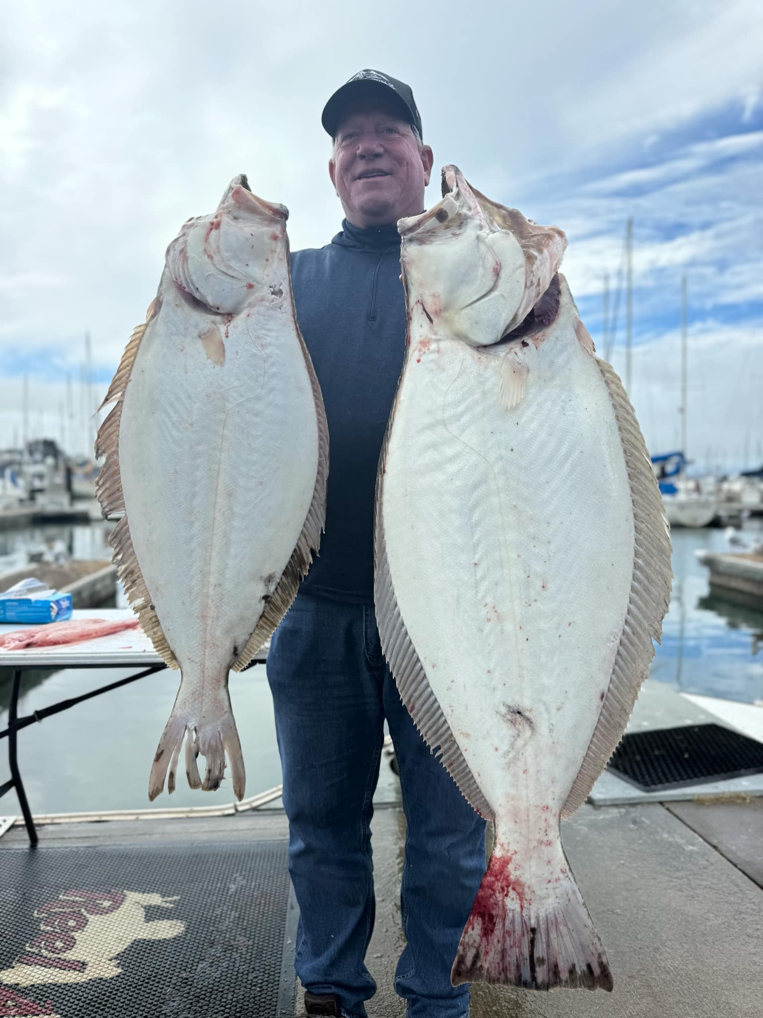 An angler on the dock holding two California halibut