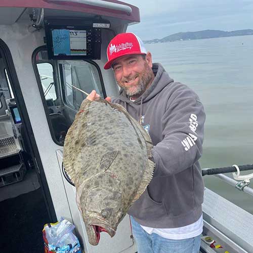 A crew member holding a California halibut beside the cabin