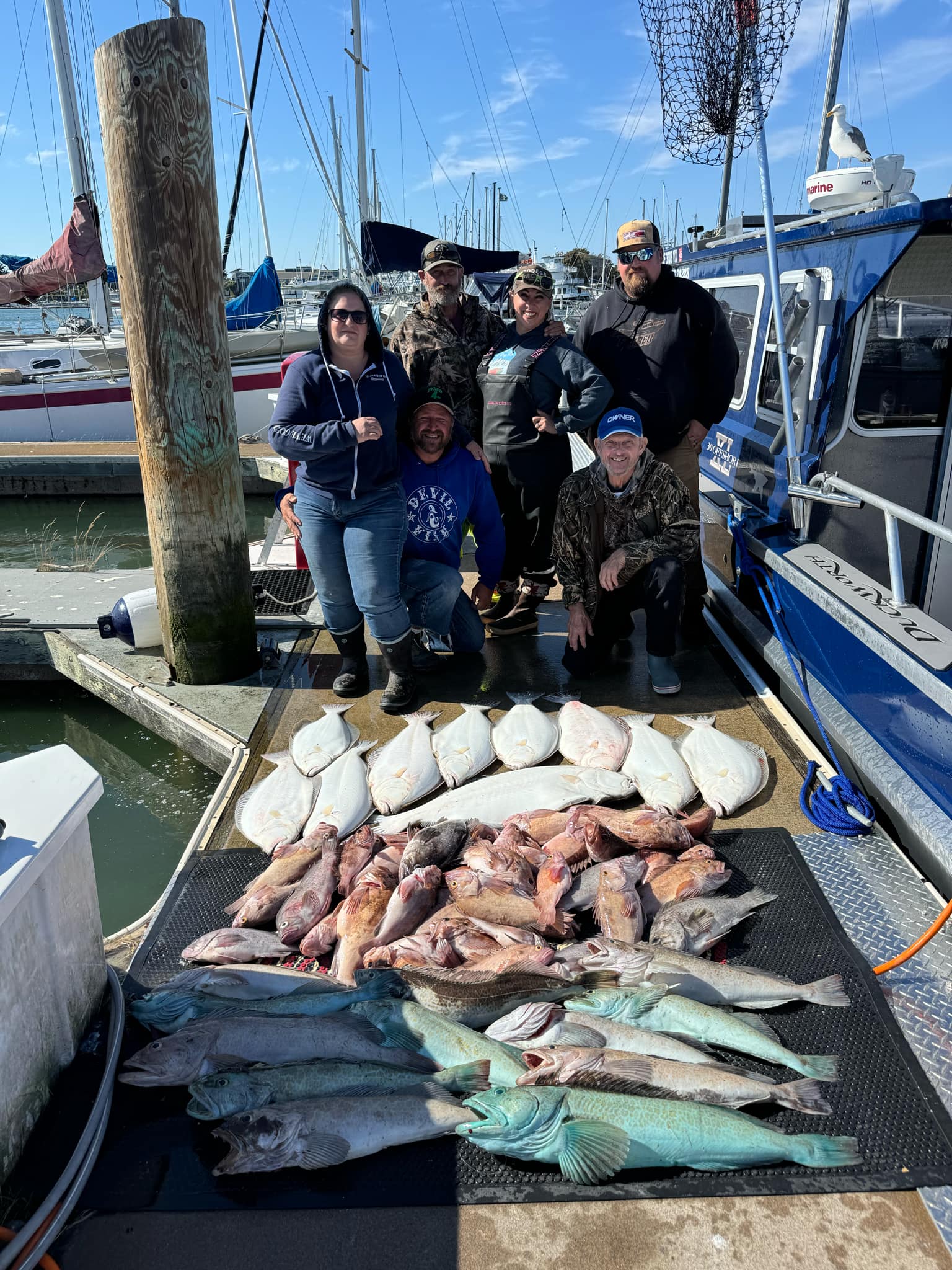 A group on the dock behind a deck of rockfish, halibut and blue-green lingcod