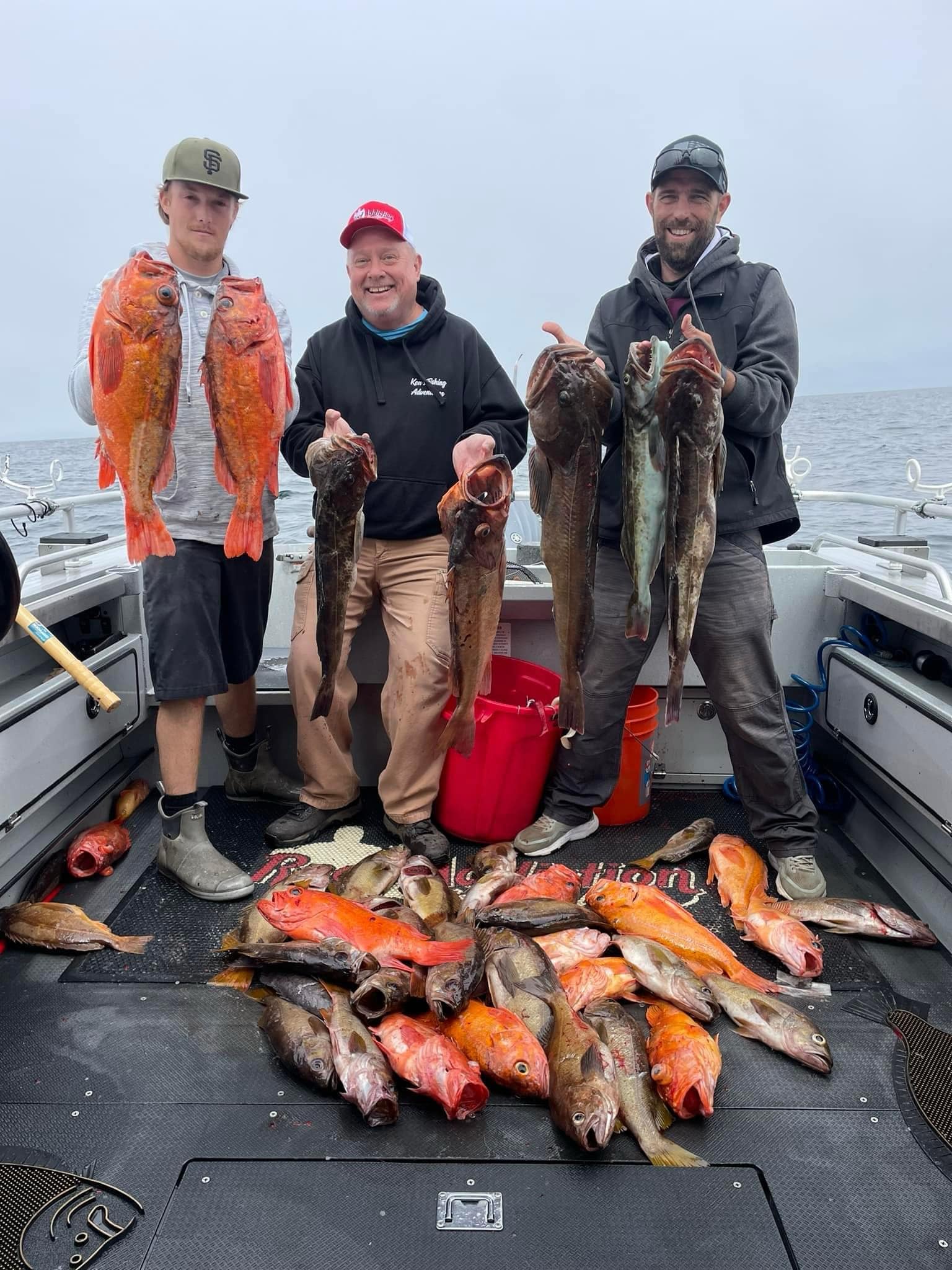 Three anglers holding lingcod and vermilion rockfish over a deck full of rockfish
